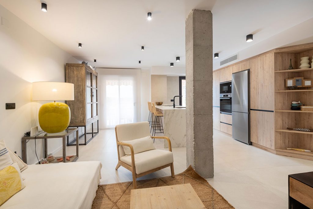 Diseño de cocina a medida con baldas de madera natural rechapada para dar continuidad y prolongar el espacio entre la cocina y el comedor.