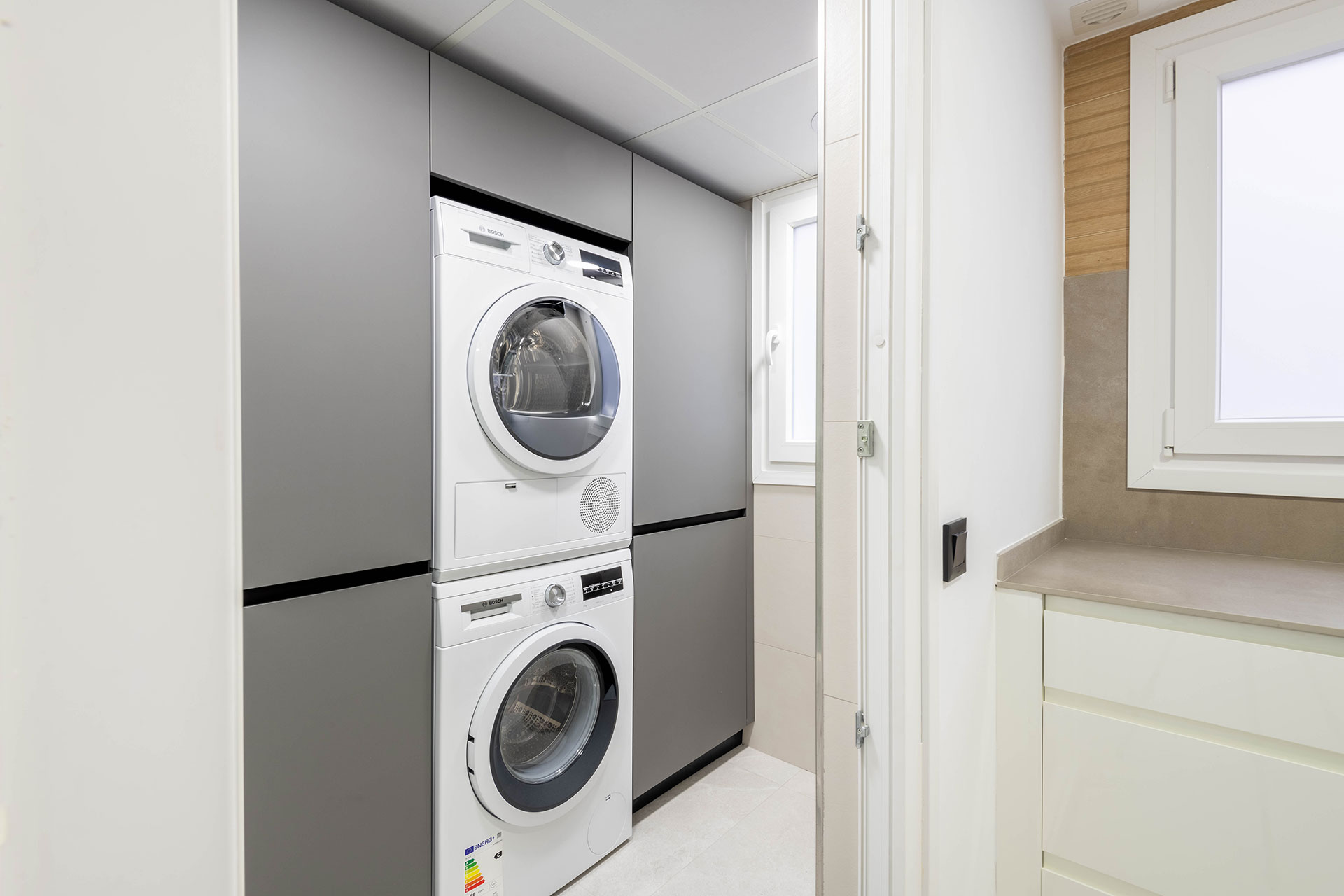 Diseño de cocina con lavandería integrada, lavadora y secadora Bosch, y armarios adicionales para caldera y otros útiles.